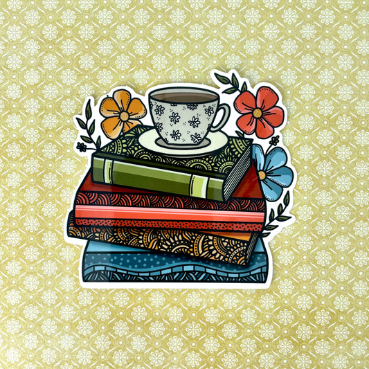 Illustrated sticker of a stack of books with a coffee cup and florals. Laying on top of a yellow background.