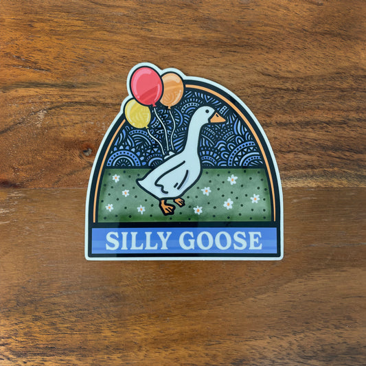 Sticker of a goose with balloons laying on a wooden surface, featuring the text 'SILLY GOOSE'