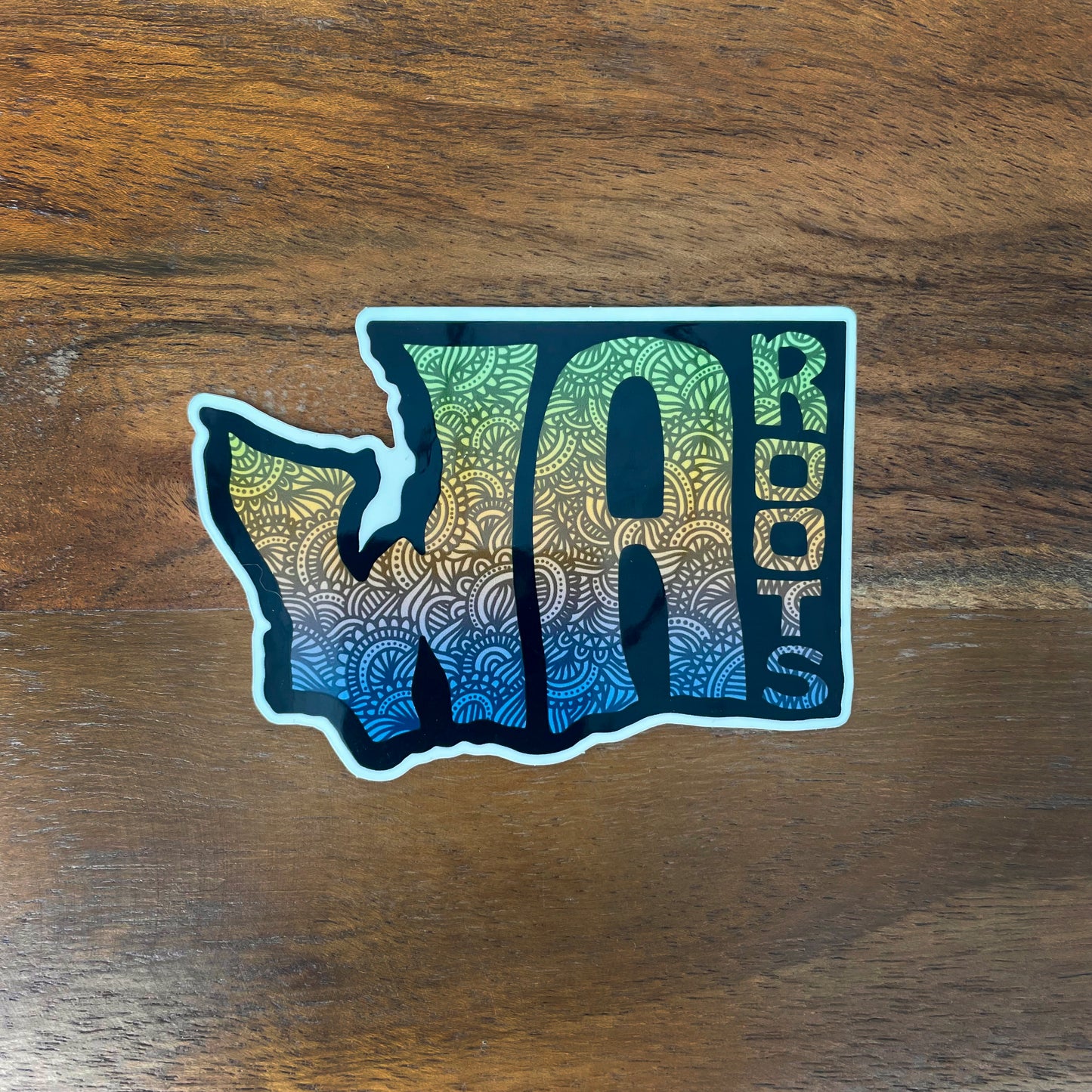 WA state roots sticker laying on a wooden surface.