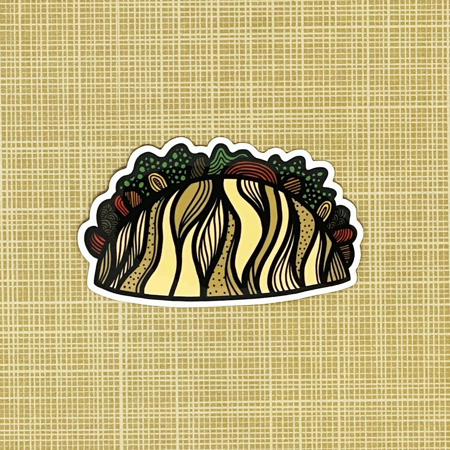 An illustrated taco made into a vinyl sticker laying on a patterned background