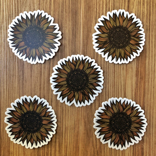 Very detailed sunflower drawing made into die-cut stickers. A group of five laying on a wooden surface.