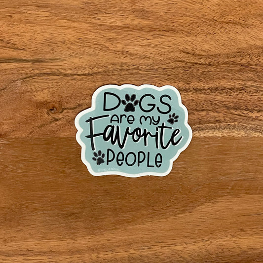 "Dogs are my favorite people" illustrated for a sticker with paw prints. Laying on a wooden surface.