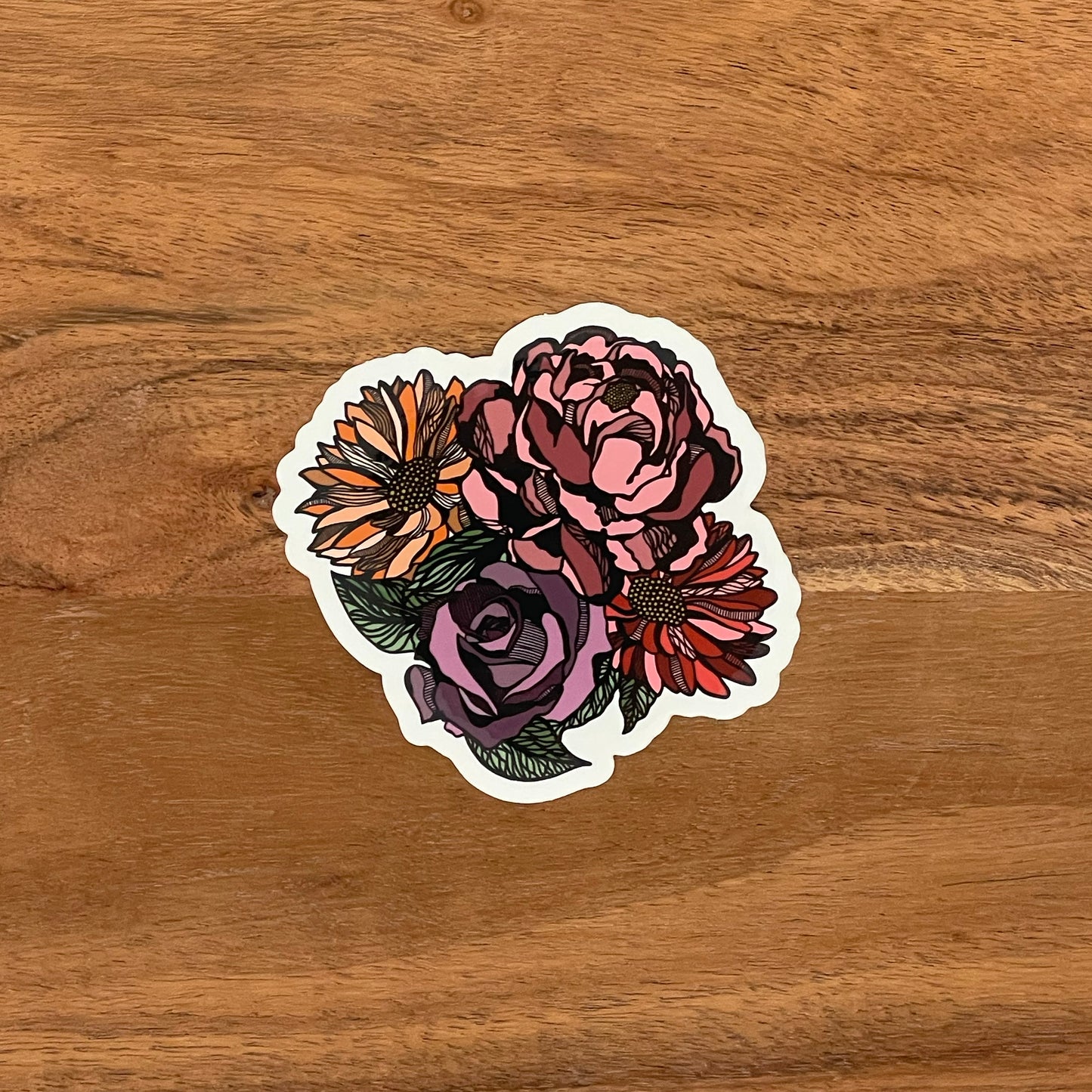 A floral bouquet sticker with red, pink, orange and purple flowers. Laying on a wood surface.