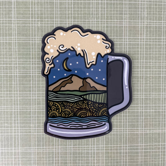 Sticker of a beer mug with Northwest Washington landscape design inside the mug laying on a patterned background.