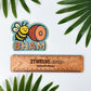 Sticker with bee and ham illustration with 'BHAM' under it. Laying next to a wooden ruler with '2Twelve Design', surrounded by green leaves. Bellingham, Washington sticker.