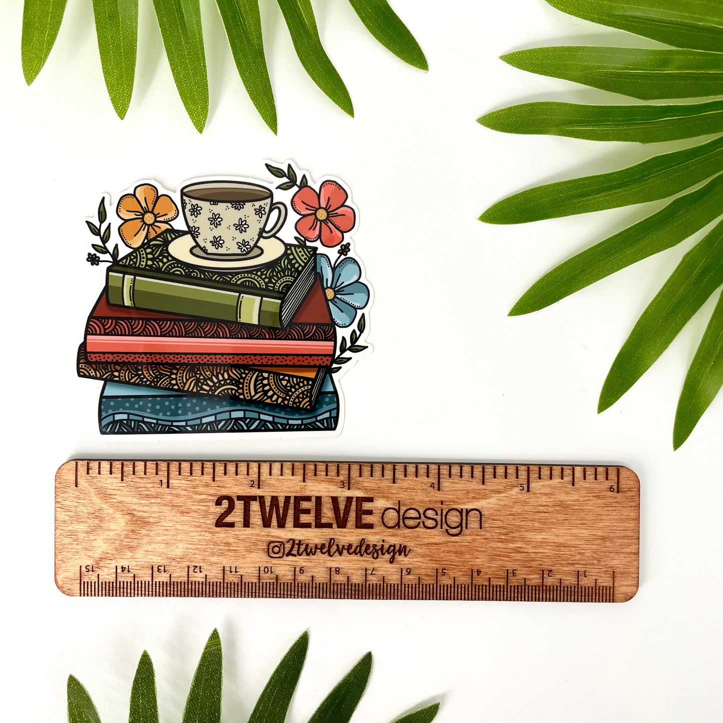 Decorative sticker of books and a coffee cup with flowers, surrounded by leaves and accompanied by a wooden ruler to show actual size.