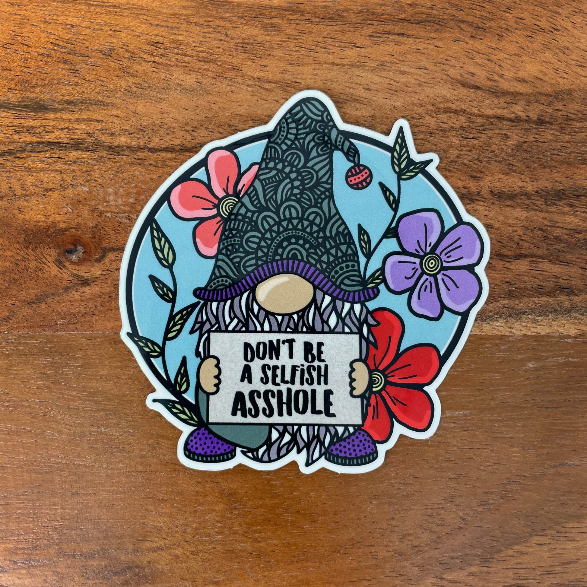 Sticker of a gnome holding a sign. Laying on a wood surface.