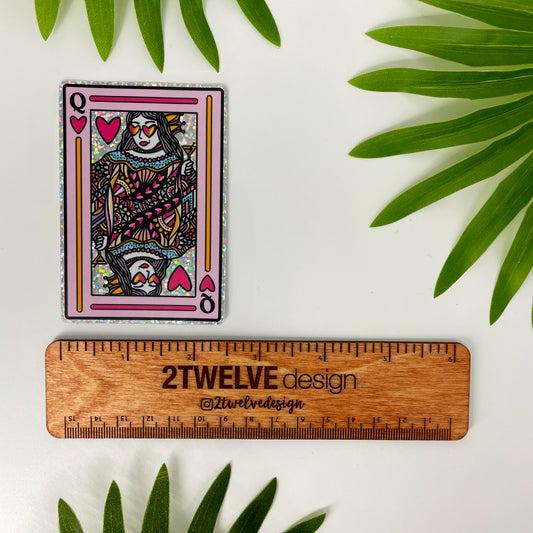 A glittery Queen of Hearts playing card sticker laying on a white background with leaves surrounding and a ruler to show actual size.