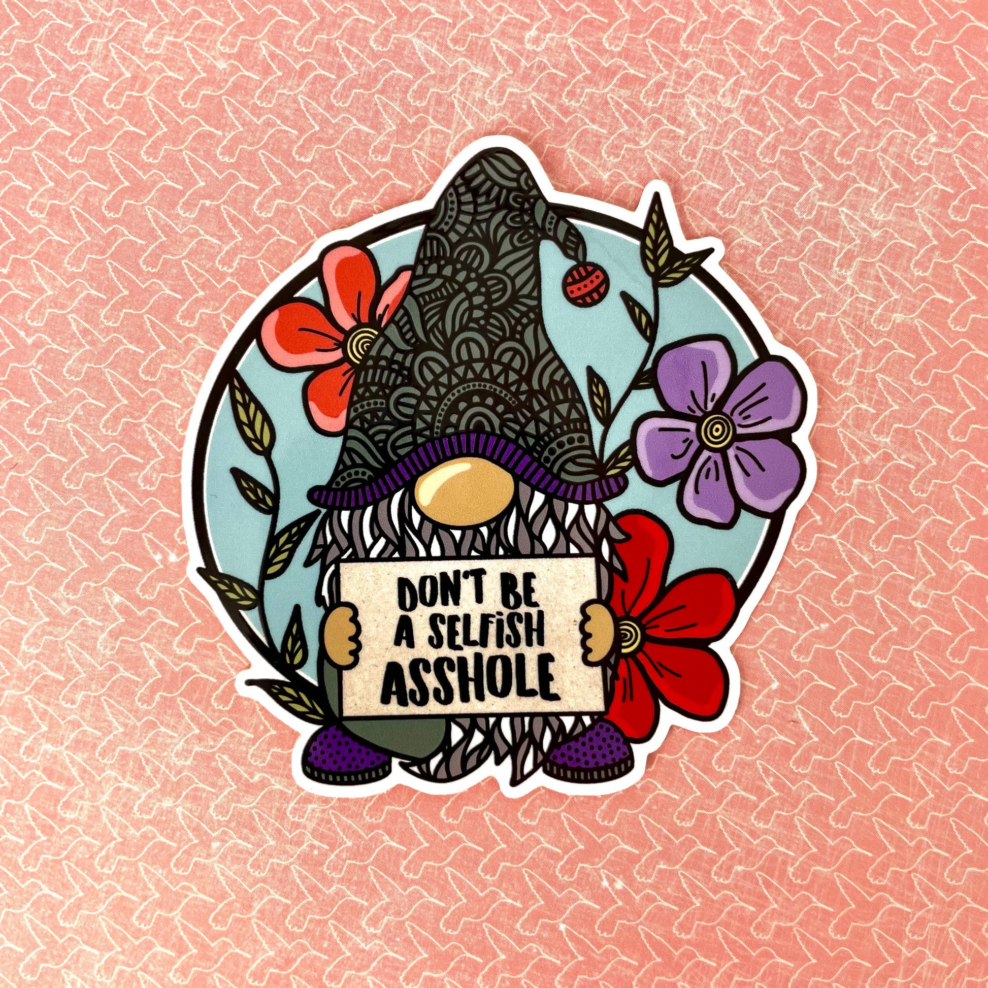 Sticker with a gnome holding a sign saying 'Don't be a selfish asshole' on a pink background.