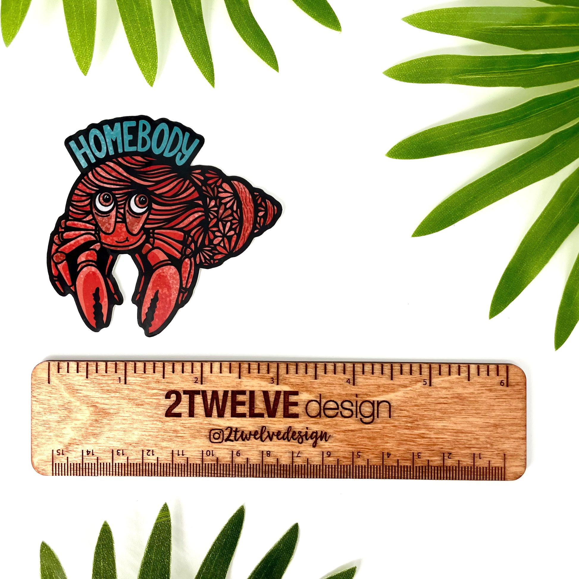 Illustration of a hermit crab with "Homebody" written above. Laying on a white background with surrounding leaves and a rule to show actual size.