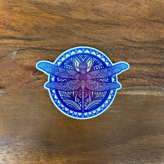 Blue and purple dragonfly mandala illustrated sticker laying on a wooden surface.
