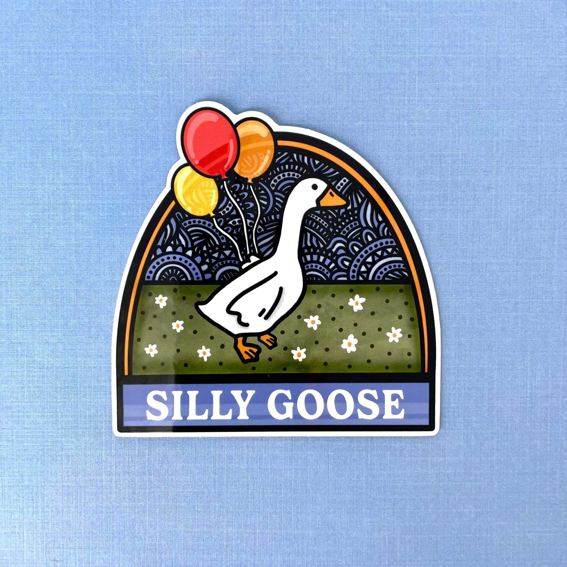 Sticker with a goose holding balloons and 'Silly Goose' text laying on a blue background