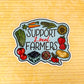 A die-cut sticker featuring the text 'SUPPORT Local FARMERS' surrounded by illustrated vegetables and fruits, shown on a yellow textured background.