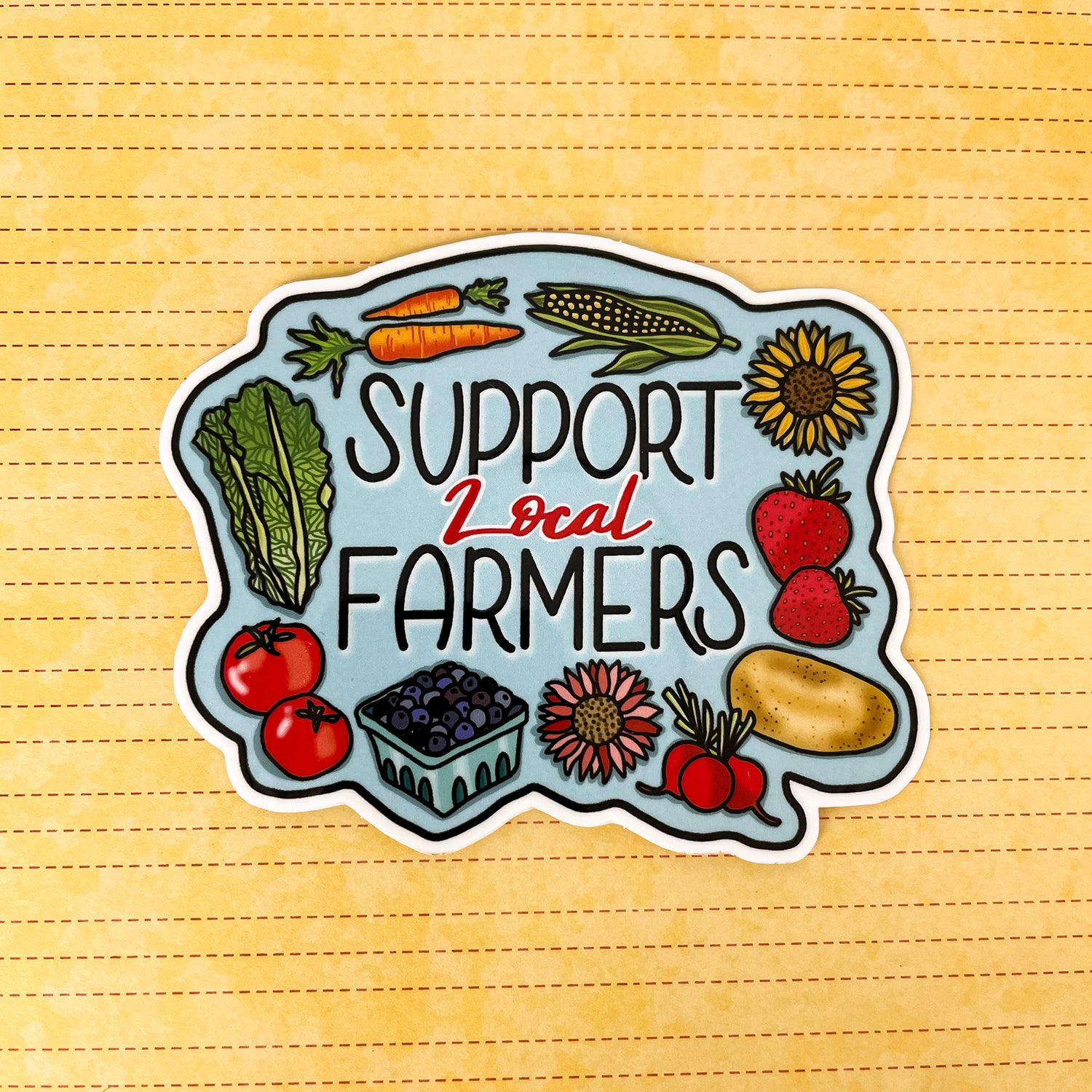 A die-cut sticker featuring the text 'SUPPORT Local FARMERS' surrounded by illustrated vegetables and fruits, shown on a yellow textured background.