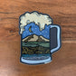 Sticker of a beer mug with Northwest Washington landscape design inside the mug laying on a wooden texture background.