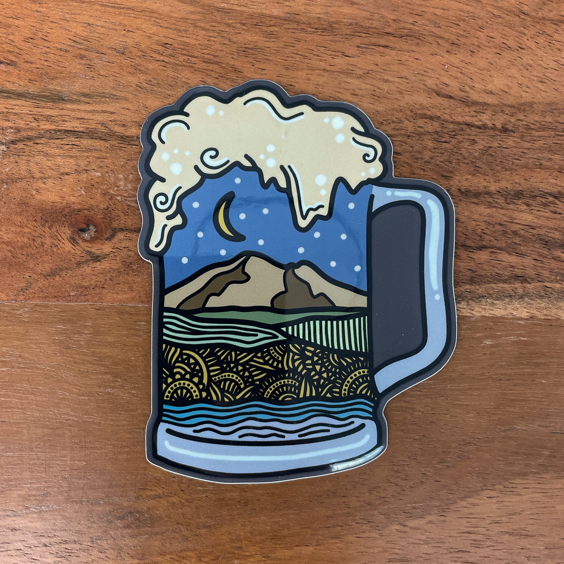 Sticker of a beer mug with Northwest Washington landscape design inside the mug laying on a wooden texture background.
