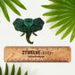 A hand illustrated elephant with intricate details made into a vinyl sticker. Laying on a white surface above a wooden "2Twelve Design" ruler. Surrounded by palm leaves