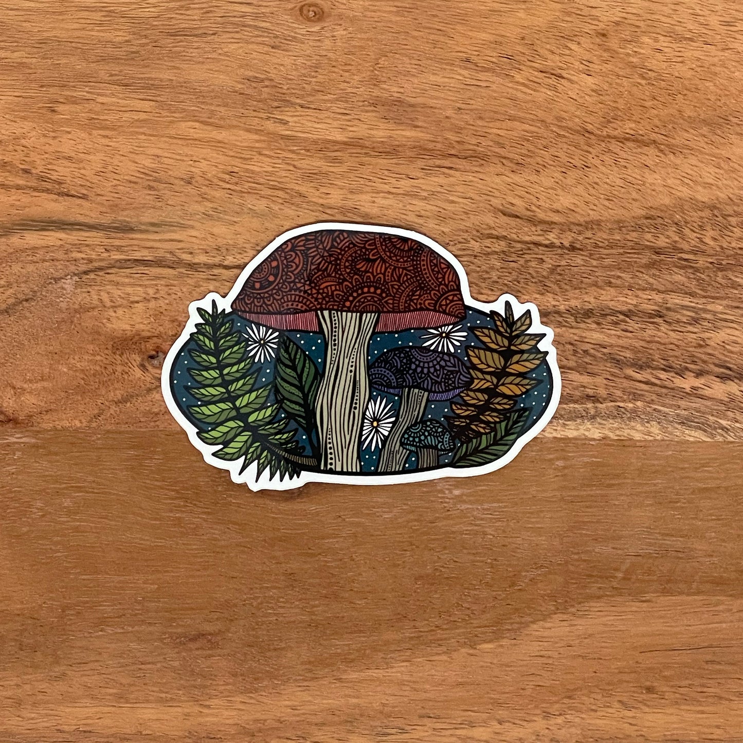 Detailed mushroom illustration made into a die-cut vinyl sticker. Laying on a wooden surface.