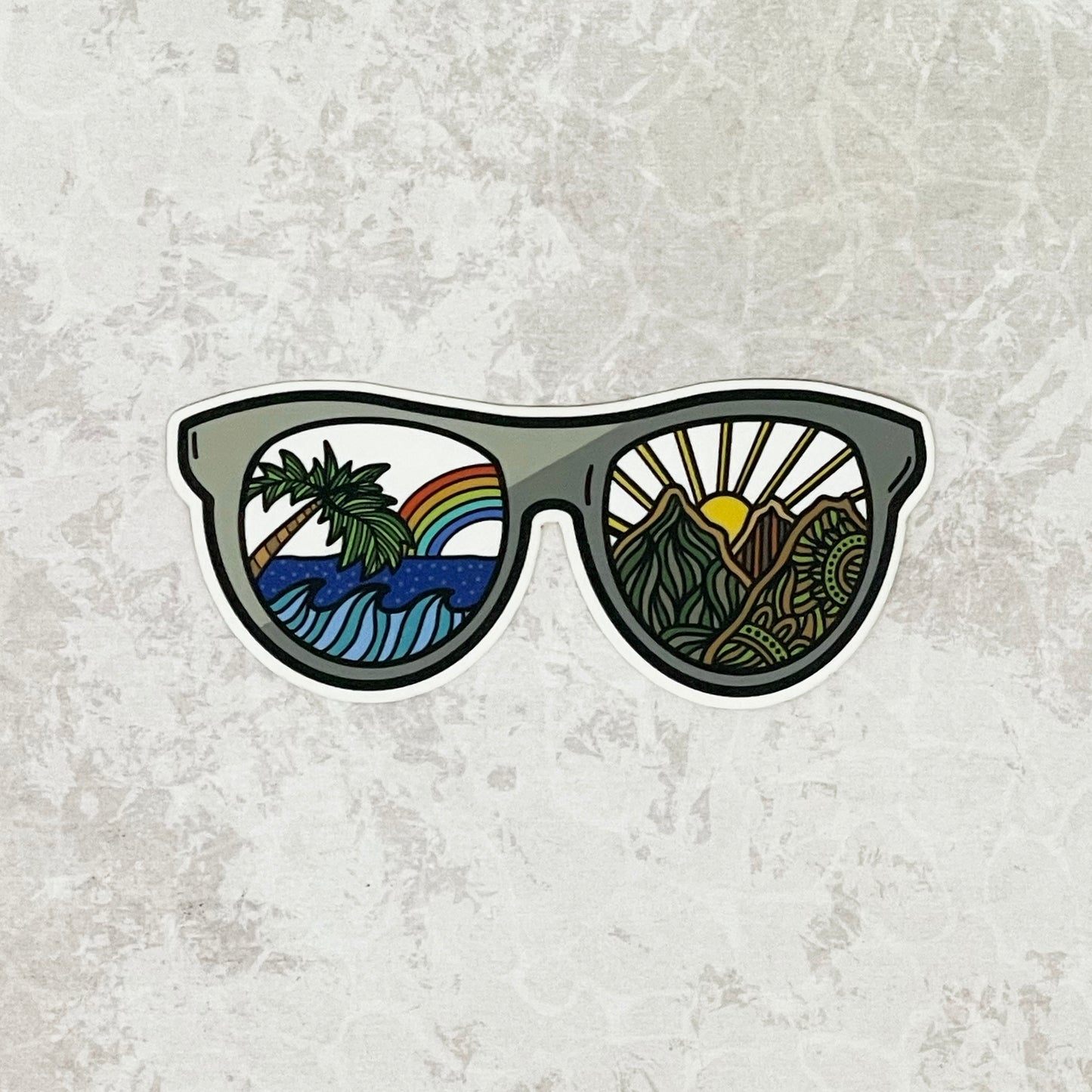 Sea to mountain designed sunglasses laying on a gray textured surface.