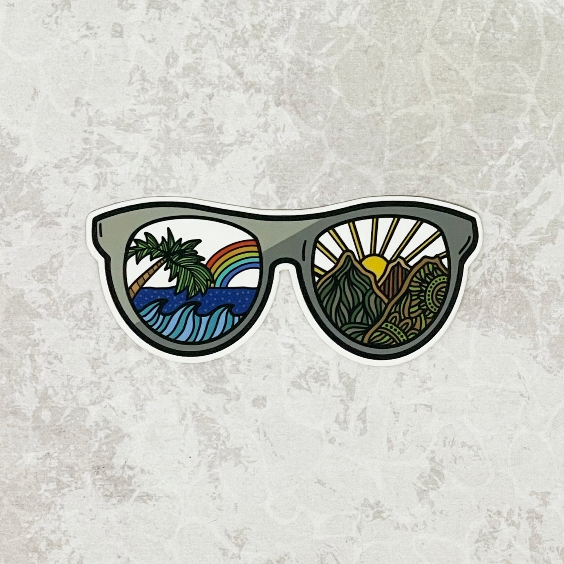Sea to mountain designed sunglasses laying on a gray textured surface.