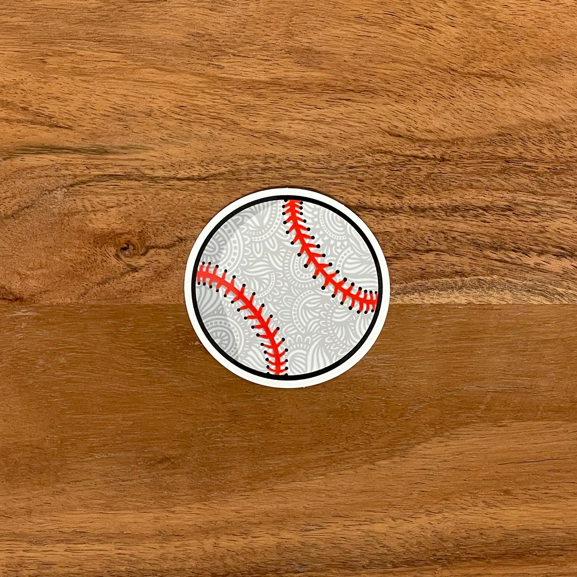 An illustrated baseball turned into a small sticker. Laying flat on a wooden surface.