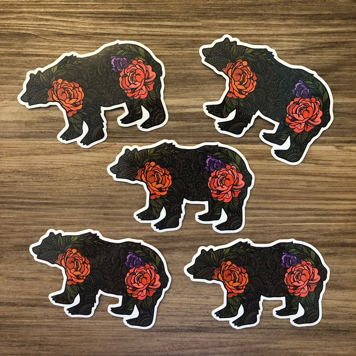 A group of hand illustrated bear stickers laying on a wooden surface. 
