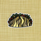 An illustrated taco made into a vinyl sticker laying on a patterned background