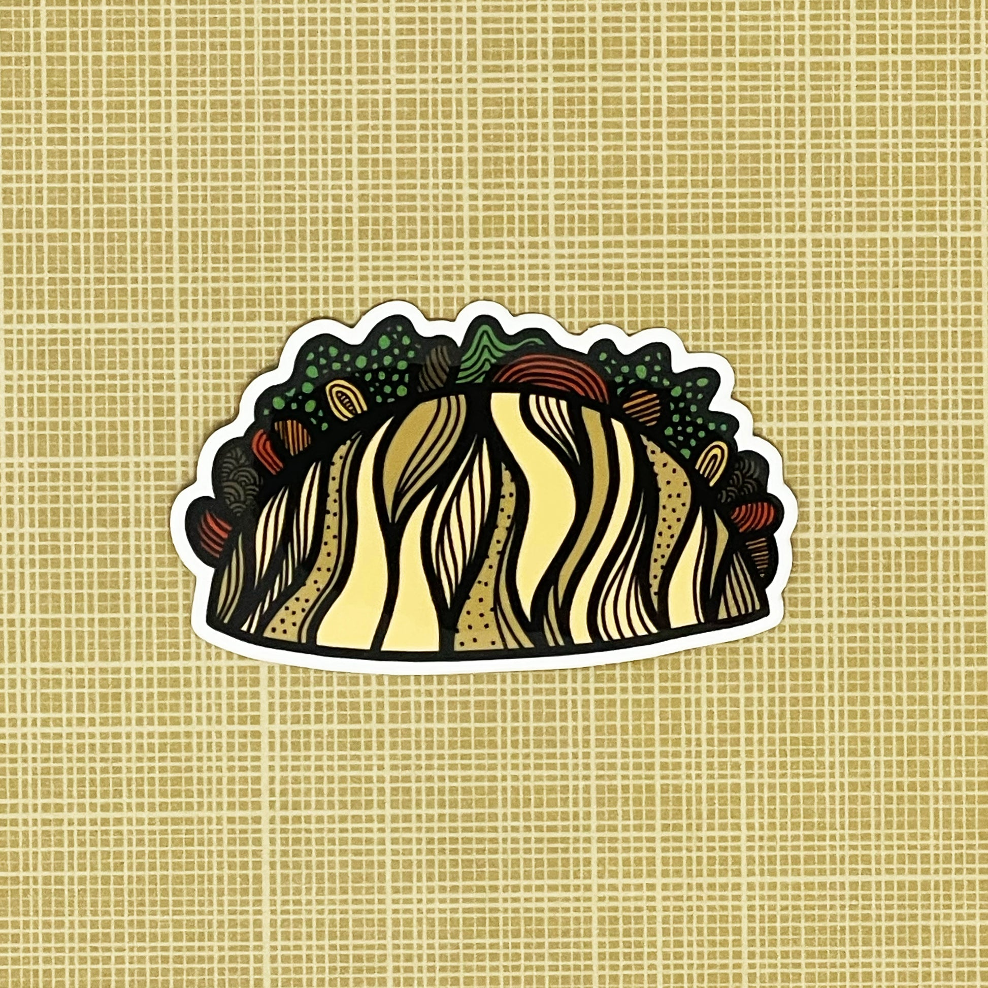 An illustrated taco made into a vinyl sticker laying on a patterned background