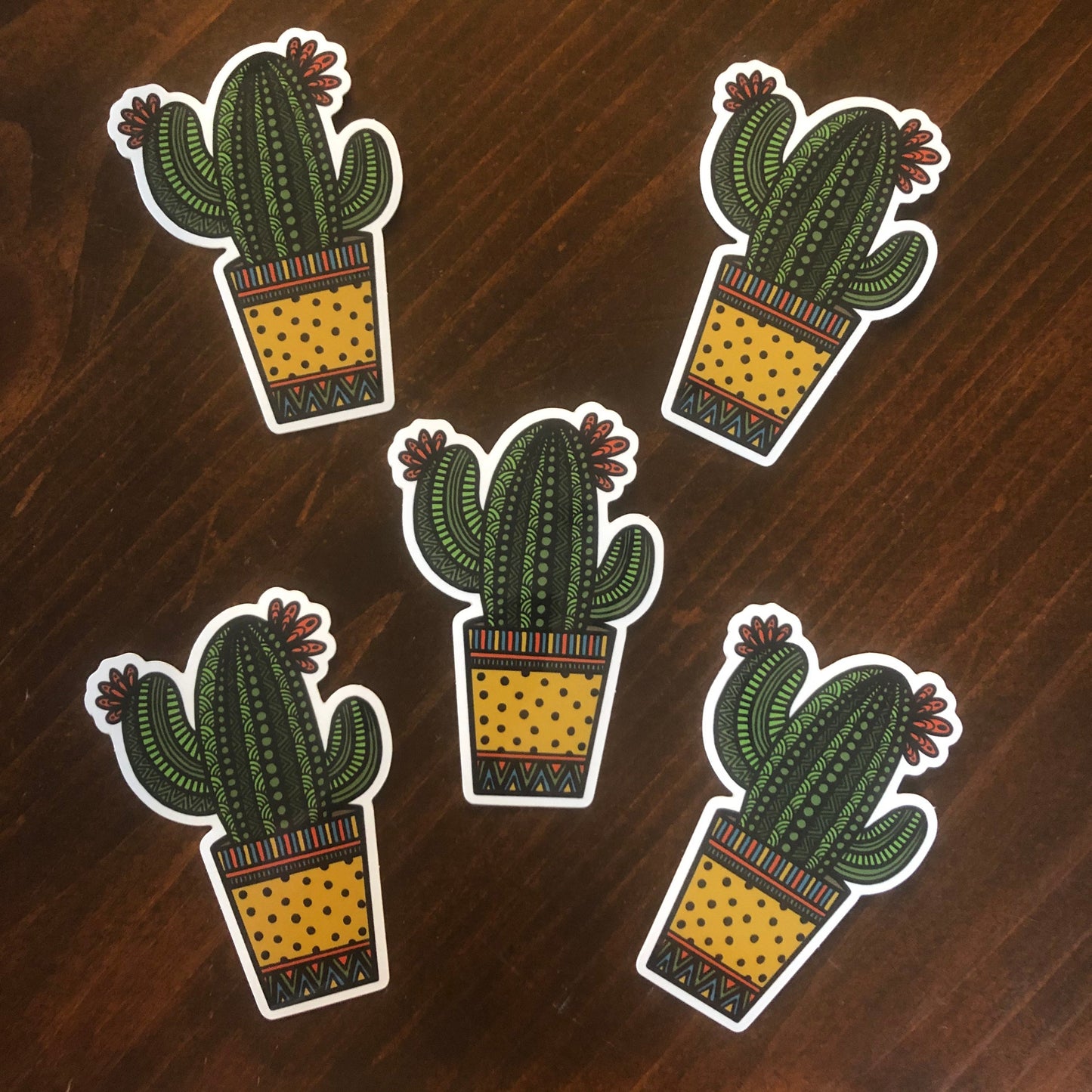 Multiple cute and spunky potted cactus stickers laying on a wooden surface.