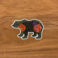 A cute illustrated bear drawing made into a vinyl sticker. Laying on a wooden surface.
