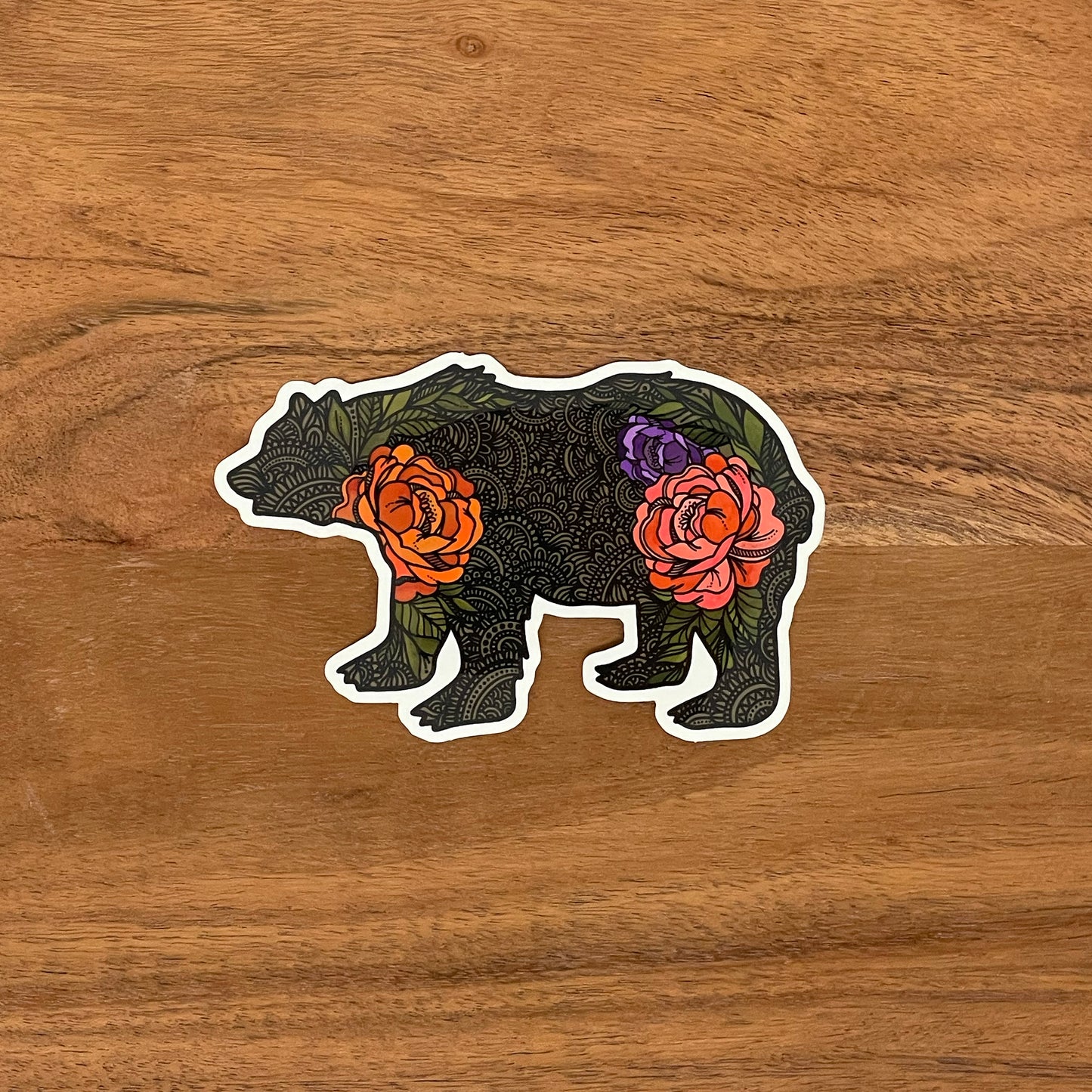 A cute illustrated bear drawing made into a vinyl sticker. Laying on a wooden surface.
