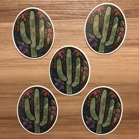 A cute cactus illustration made into an oval die-cut sticker. A group of 5 stickers laying on a wooden surface.
