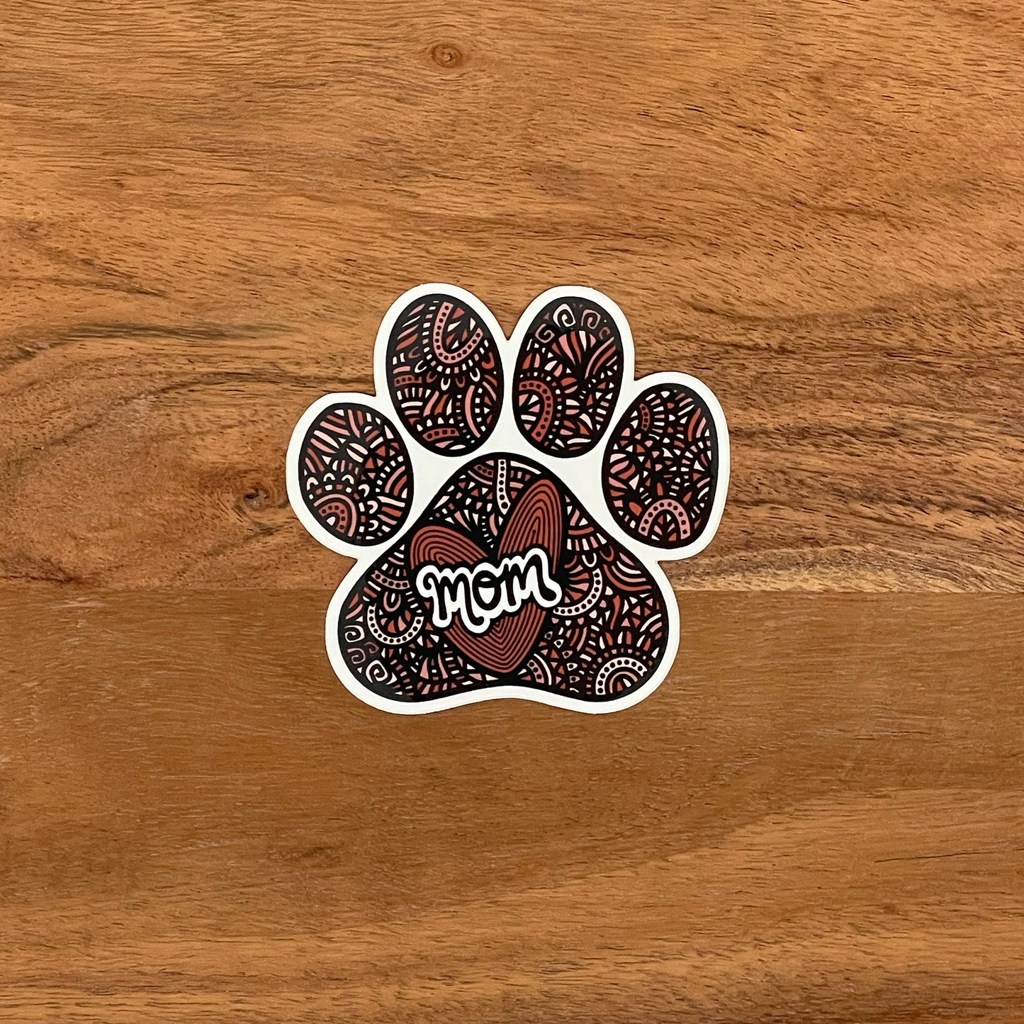 A cute detailed dog mom paw print illustration made into a die-cut sticker. Laying on a wooden surface.