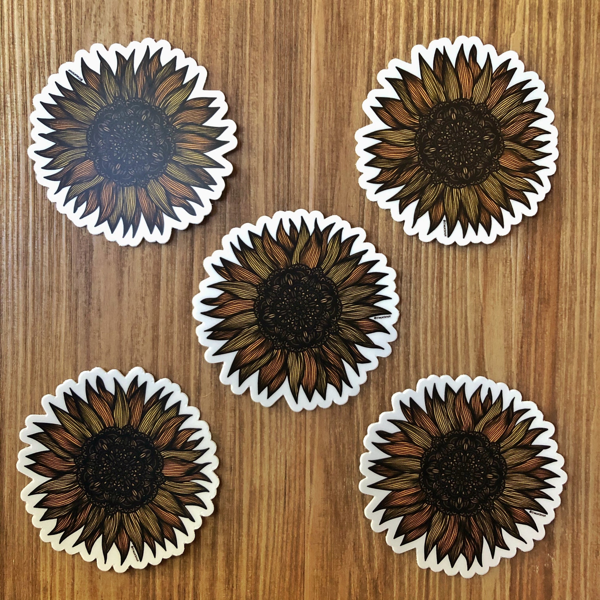 Very detailed sunflower drawing made into die-cut stickers. A group of five laying on a wooden surface.