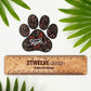 A hand-drawn paw print illustration in a black, red, and pink color palette, designed as a vinyl, waterproof die-cut sticker with the word 'Mom' incorporated into the design. Laying on a white background with a "2Twelve Design" ruler to show size. All surrounded by green palm leaves.