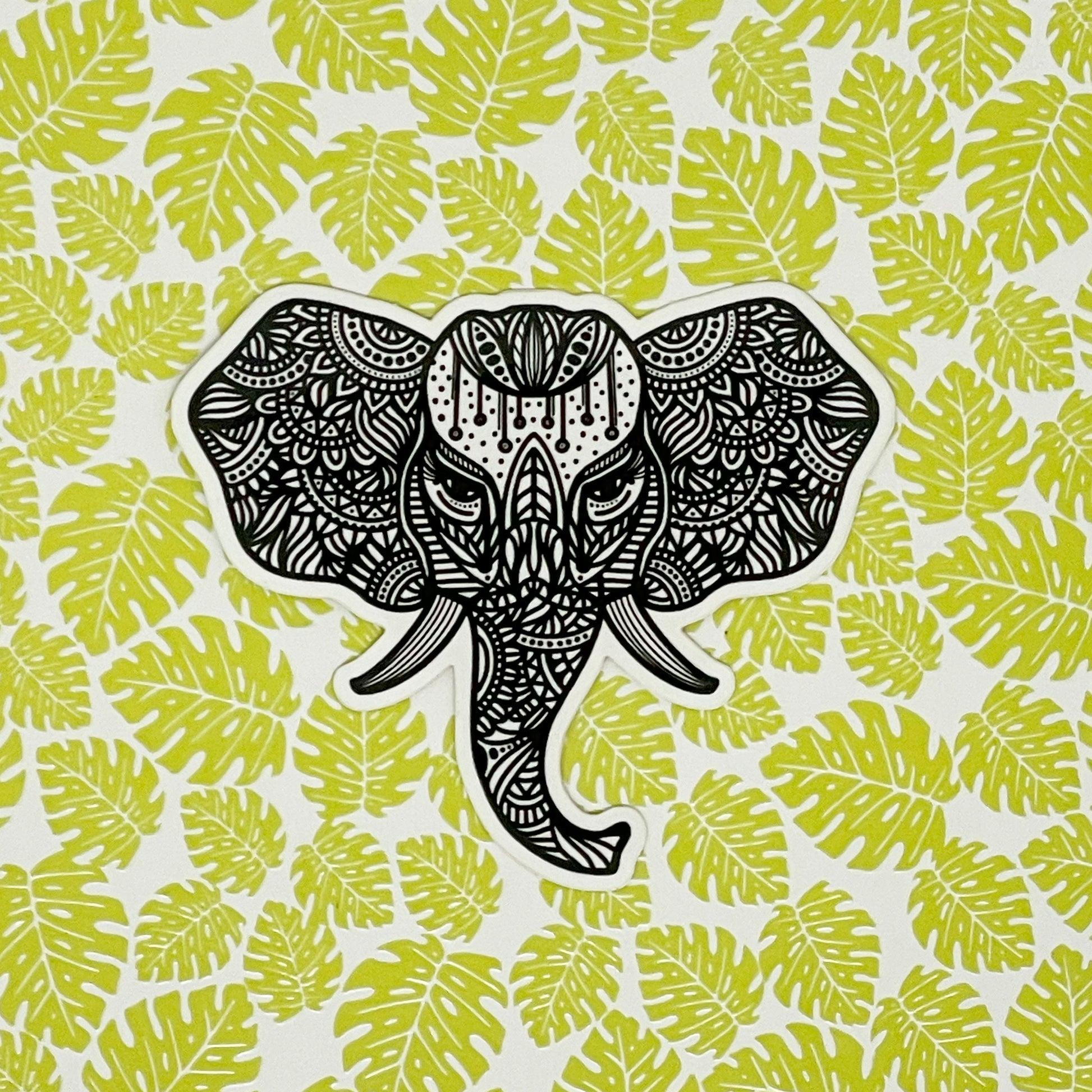 Intricate illustration of an elephant made into a vinyl sticker. Laying on a patterned tropical background.