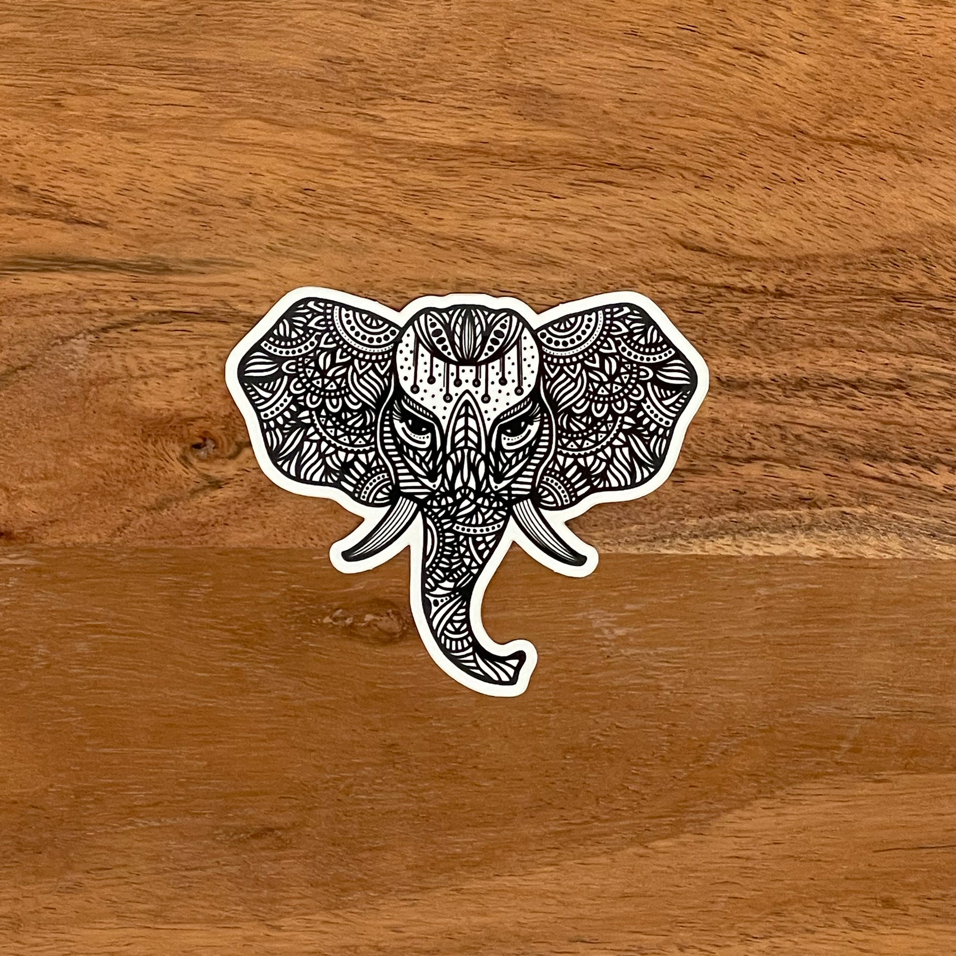An illustrated elephant made into a vinyl sticker laying on a wooden surface.