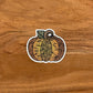 A cute, autumn pumpkin illustration with intricate details turned into a vinyl sticker. Laying on a wooden surface.