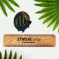 A very detailed fish and mountain illustration made into a die-cut sticker. Laying on a white background above a "2Twelve Design" ruler, surrounded by palm leaves.