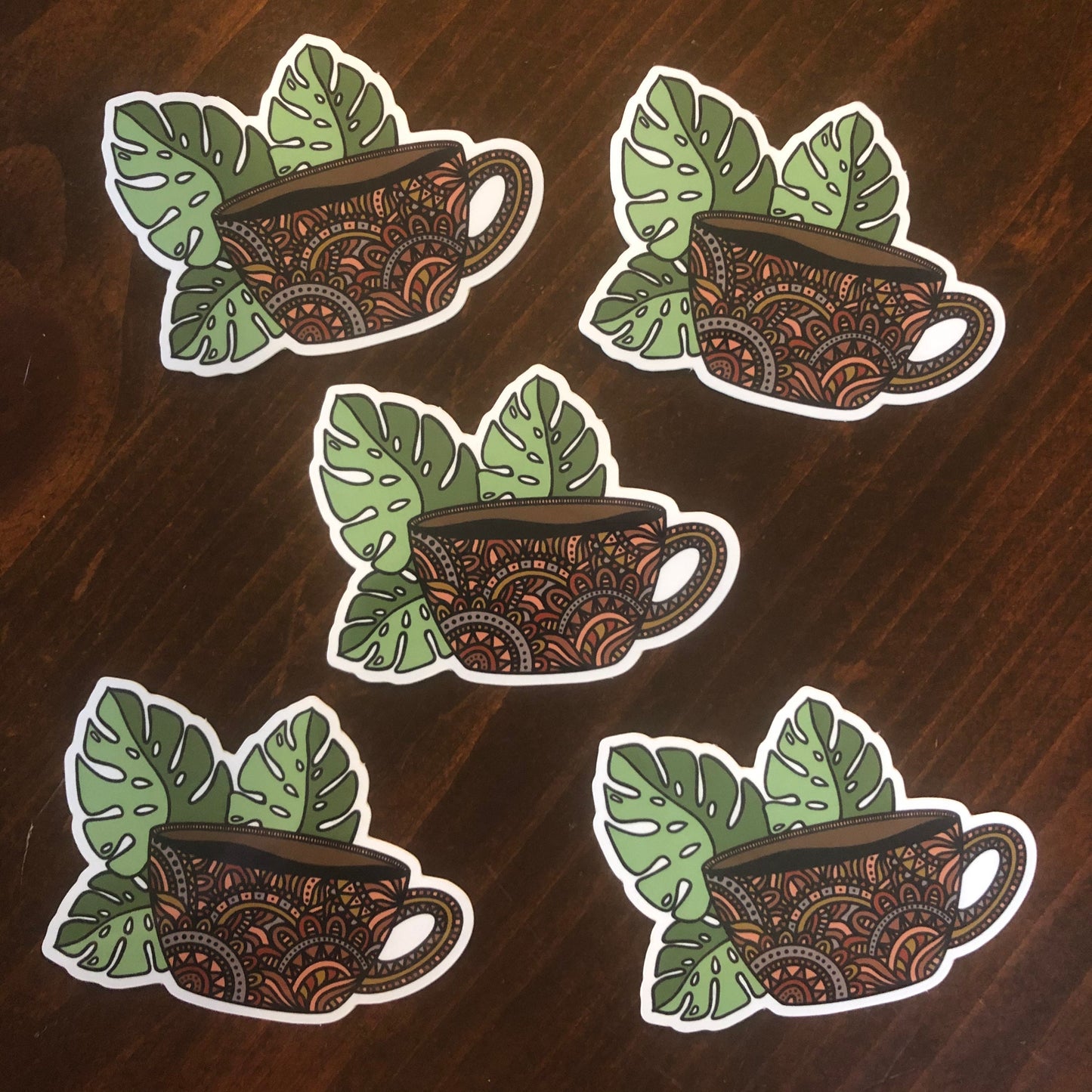 Five die-cut vinyl stickers featuring a hand-drawn illustration of a coffee mug with monstera leaves, laying on a wooden surface.