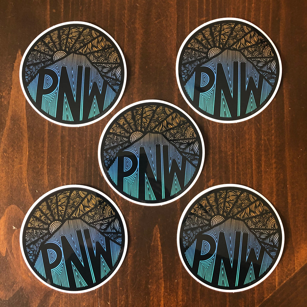 A group of give pacific northwest stickers laying on a wooden surface.