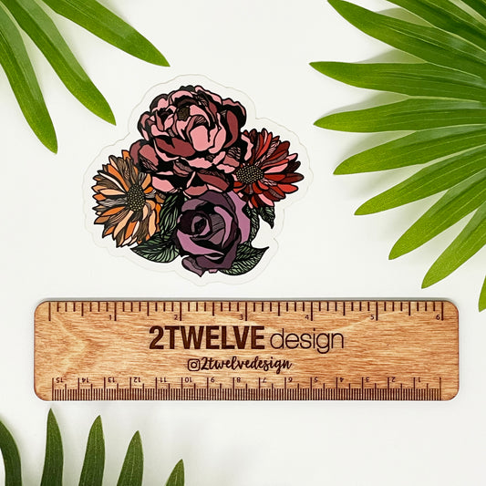 A cute flower bouquet drawing made into a die-cut sticker. Laying on a white background surrounded by palm leaves. "2Twelve Design" ruler to show size.