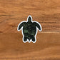 A green turtle (honu) sticker laying on a wood surface