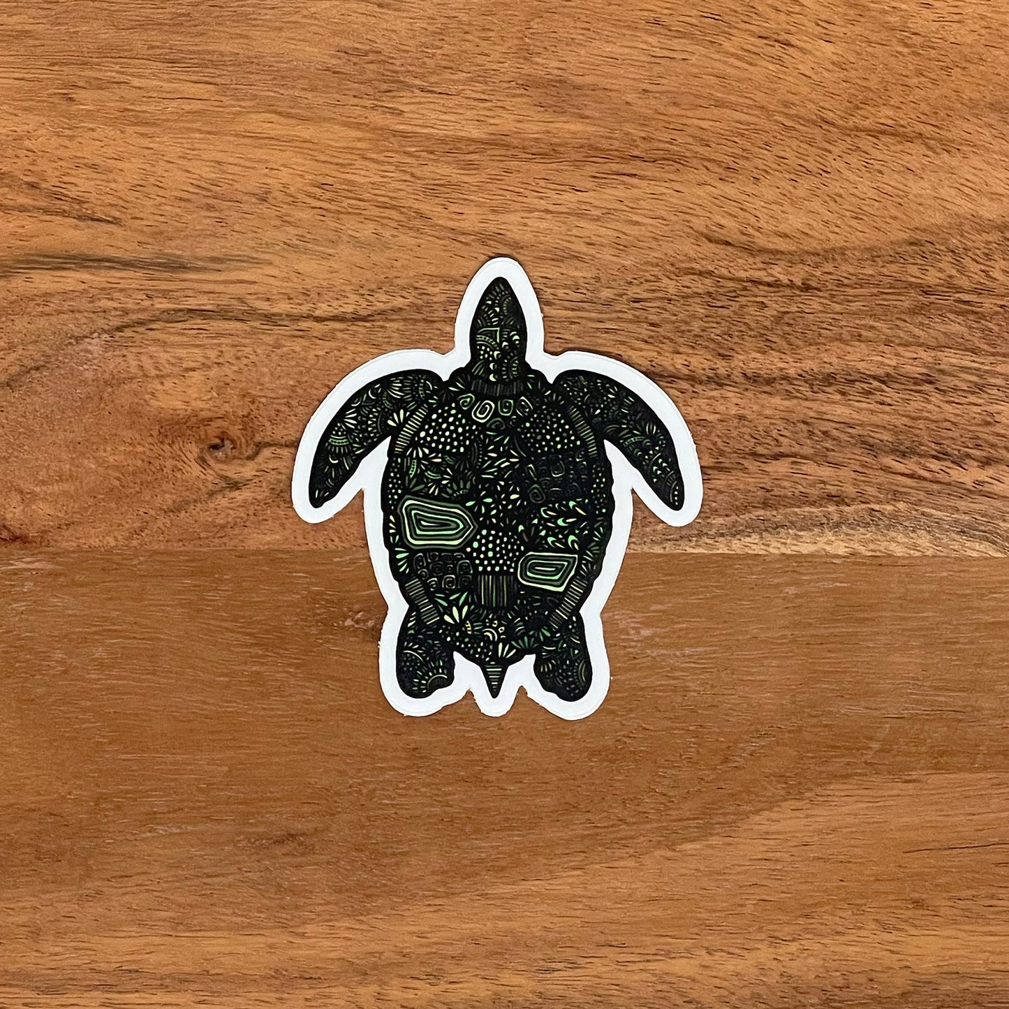 A green turtle (honu) sticker laying on a wood surface