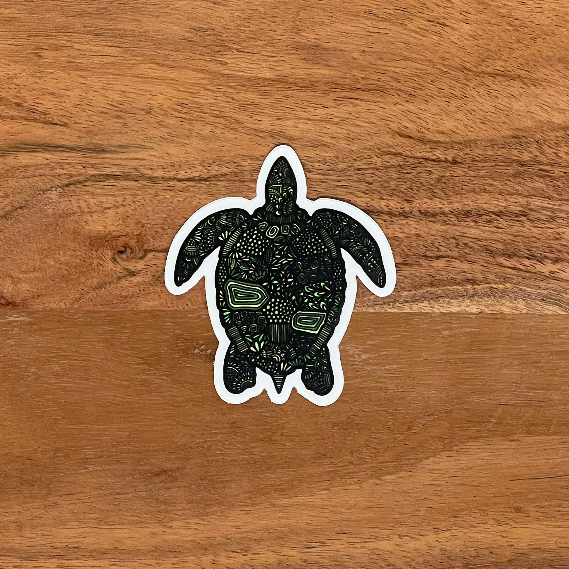 A green turtle (honu) sticker laying on a wood surface