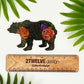 An intricate illustrated bear made into a vinyl sticker. Laying on a white surface above a "2Twelve Design" wooden ruler. Surrounded by palm leaves.