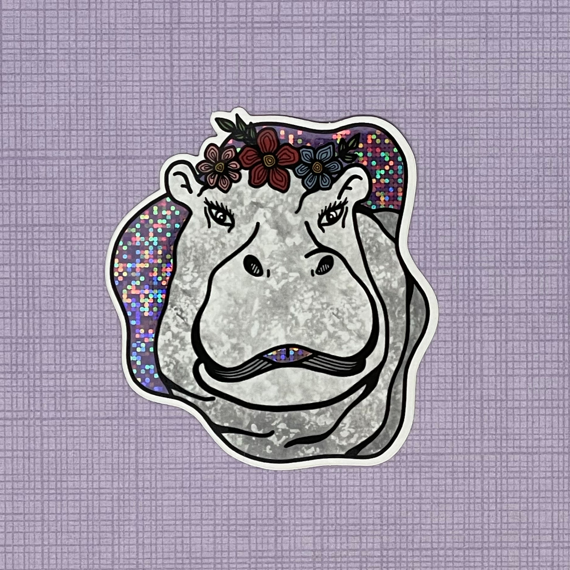 A fun and sassy hippo illustration made into a glittery sticker. Laying on top of a purple pattern background. 