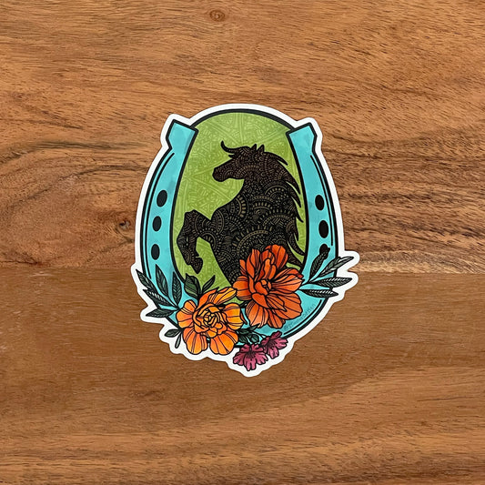 A horse, floral and lucky horseshoe illustration made into a die-cut sticker. Laying on a wooden surface.