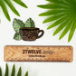 A die-cut vinyl sticker featuring a hand-drawn illustration of a coffee mug with monstera leaves laying on a white background above a "2Twelve Design" ruler, surrounded by palm leaves.