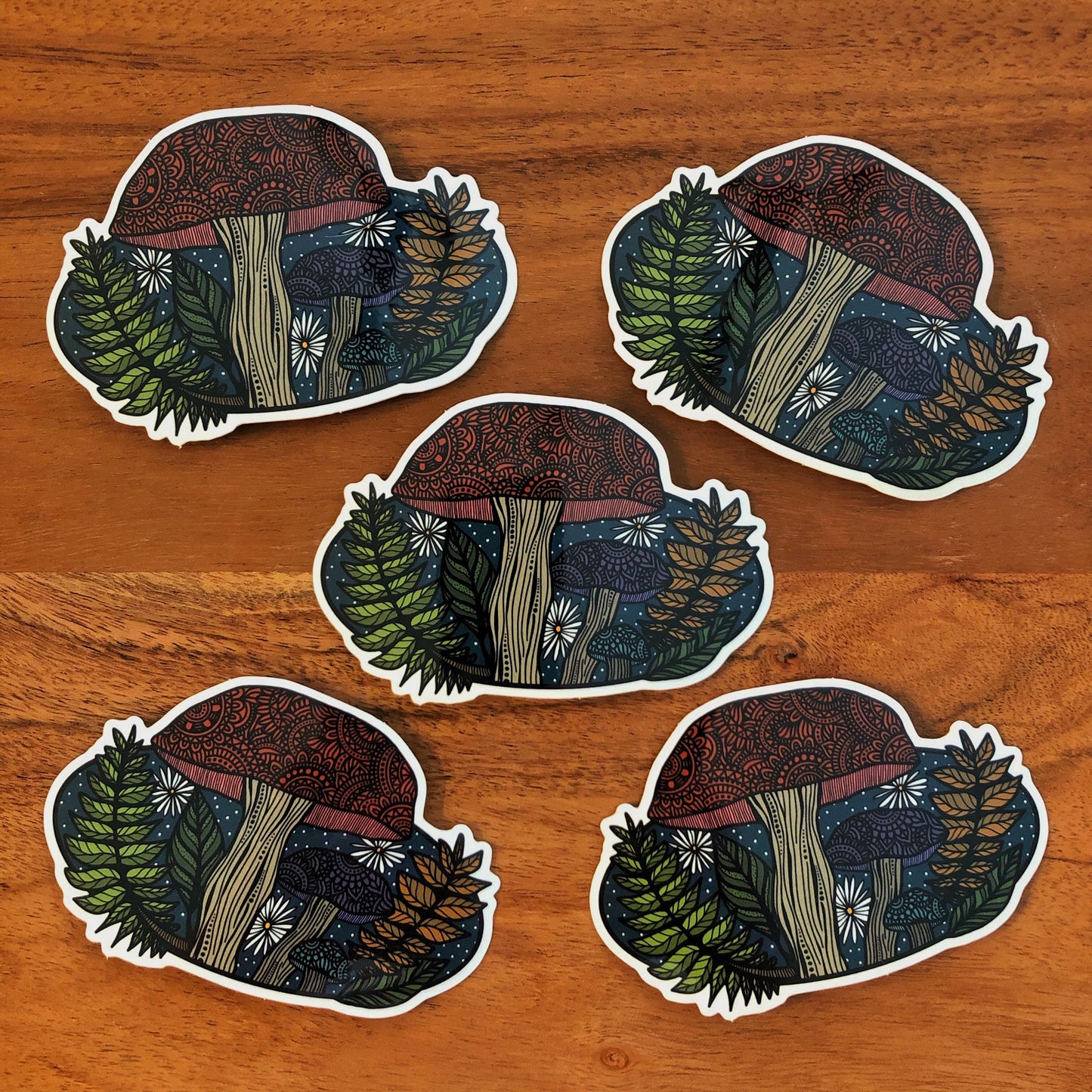A Pacific Northwest inspired mushroom illustration made into a vinyl die-cut sticker. Five stickers laying on a wooden surface.